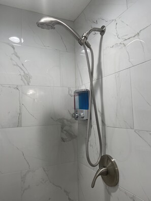 A shower with a handheld showerhead and a handheld hose, mounted on a wall with white marble tiles. - La Palma in Port Richey (Port Richey)