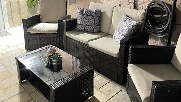 Un'area patio con mobili in vimini, tra cui un divano e poltrone, un tavolino in vetro con una pianta e una finestra vista.