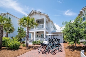 Stunning two-story home surrounded by lush greenery, featuring a spacious balcony and driveway with golf cart and bicycles.