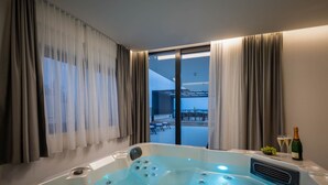 Ein modernes Badezimmer mit einer großen Badewanne, ein Balkon mit Sitzgelegenheit im Freien und eine Champagnerflasche auf der Ablagefläche.