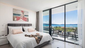 Ein modernes Schlafzimmer mit einem großen Bett, Meerblick und einem Balkon mit Gartenmöbeln.