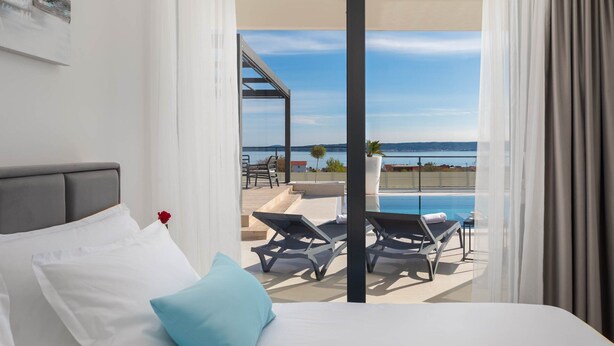 Ein Schlafzimmer mit Bett, Blick auf Pool und Strand.