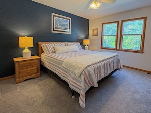 A bedroom with a bed, two bedside lamps, a nightstand, a window with blinds, and a ceiling fan. - Beach Heaven - Short walk to beach from this 6 BR Oceanside Home w/Private Pool (Southern Shores)