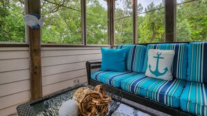 A covered porch with a striped sofa and a glass table with decorative items.