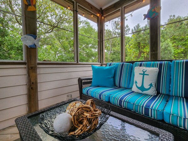 Een overdekte veranda met een gestreept bankje en een glazen tafel met decoratieve objecten.