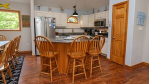 A kitchen with white cabinets, a stainless steel refrigerator, a microwave, and a wooden dining table with chairs.