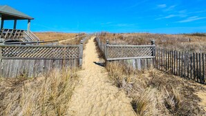 A sandy pathway leading to a wooden structure with a roof, surrounded by dry grass and a fence. - The Wright Place - 3 BR Oceanfront condo w/Ocean View from Balcony & Community Pool (Kill Devil Hills)