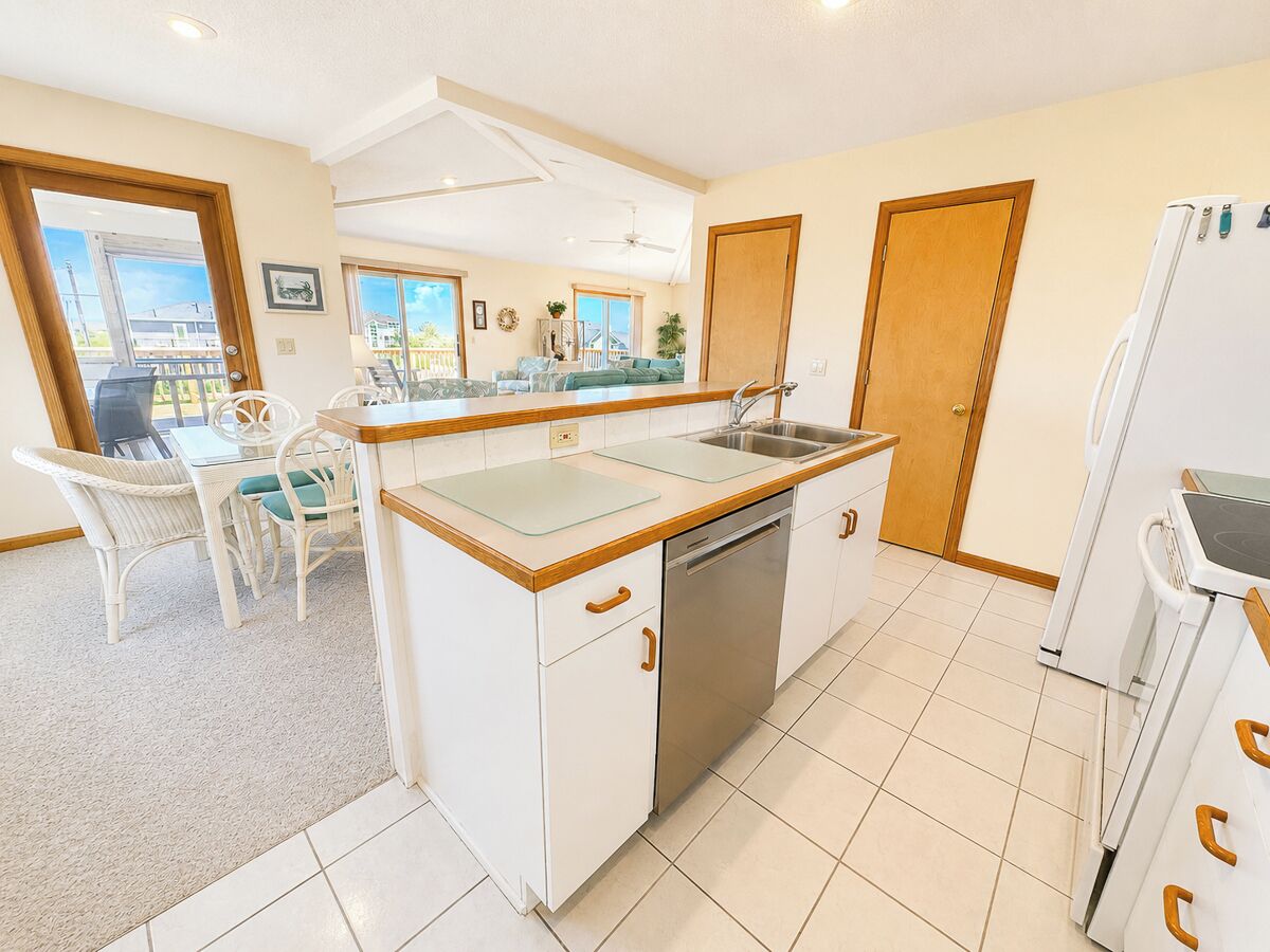 Una cocina con una isla central, un comedor con sillas, un refrigerador y un lavavajillas.