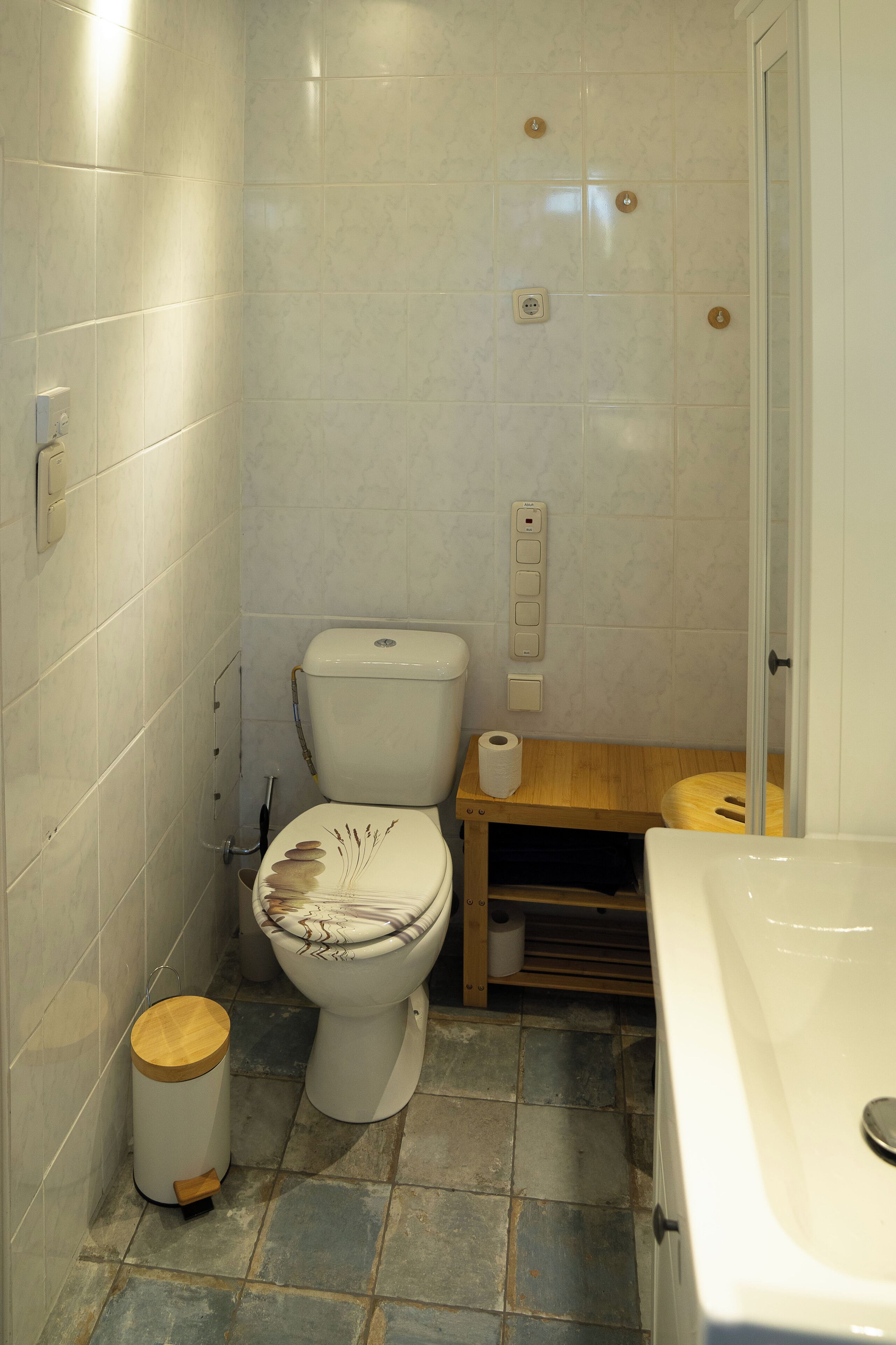 A small bathroom with a toilet, a wooden waste bin, a toilet paper holder, and a bathtub.