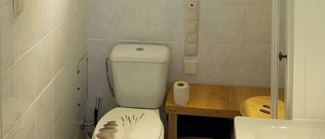 A small bathroom with a toilet, a wooden waste bin, a toilet paper holder, and a bathtub.