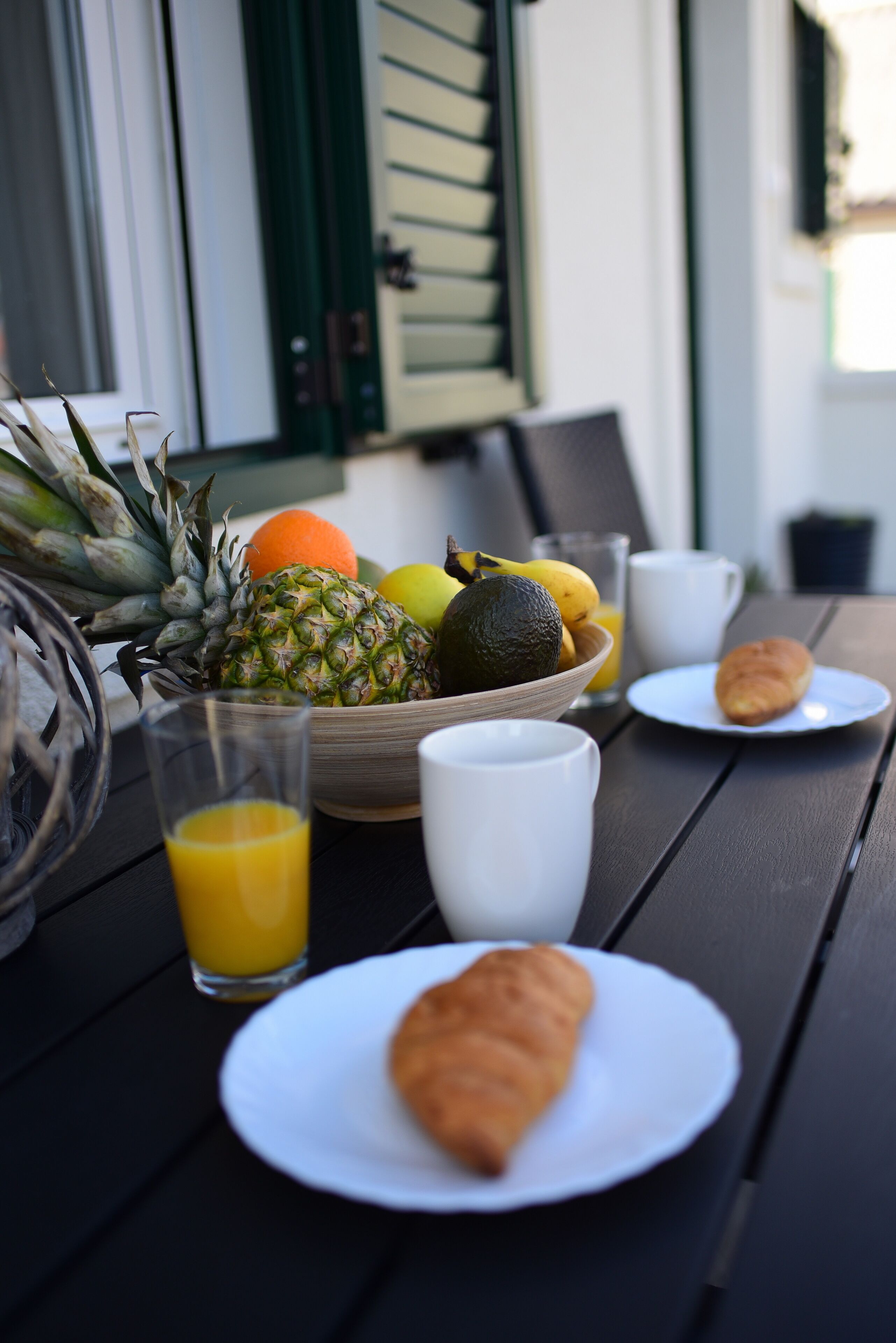 A breakfast setting with a bowl of fruits, a glass of orange juice, a croissant, and a cup on a table.