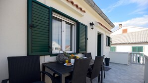 Un'area pranzo all'aperto con tavolo e sedie, una finestra con persiane e una ringhiera per il balcone.