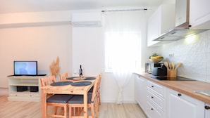 Una cucina moderna con mobili bianchi, un tavolo da pranzo in legno con sedie, una televisione e una finestra con tende leggere.
