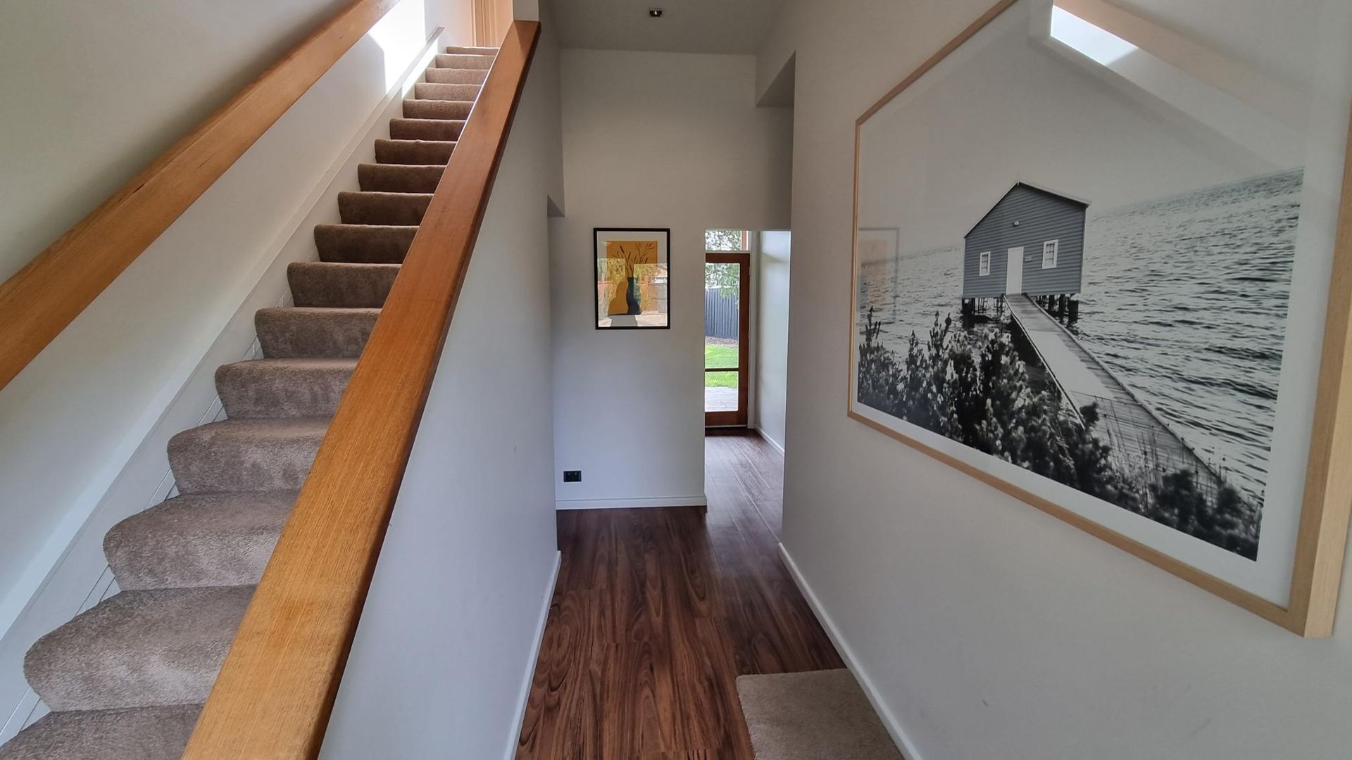 A staircase with wooden handrails and carpeted steps leading to a room with a large framed black and white photograph on the wall.