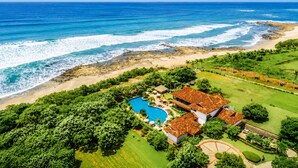 A coastal property with a swimming pool, multiple buildings, and a beach.