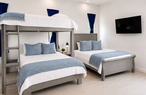 A hotel room with two bunk beds, a flat-screen TV mounted on the wall, and a bedside table with a lamp. - 2 min walk private  path to the beach . Beach club . Daily maid . Free ATVs  (Hacienda pinilla)