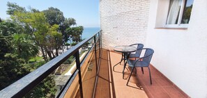 A balcony with a table and chairs, overlooking a garden and the sea. - Skol 329 – Spacious Beachfront Studio with Sea Views (Marbella)