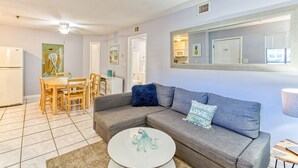 A modern living room with a grey sectional sofa, a round coffee table, and a dining area with a wooden table and chairs. - Stylish 2BD/2BA Beach Villa at Hilton Head Resort (Hilton Head Island)