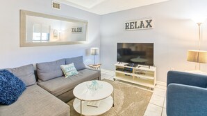 A modern living room with a grey sofa, a coffee table, a TV, and a 'RELAX' sign on the wall. - Stylish 2BD/2BA Beach Villa at Hilton Head Resort (Hilton Head Island)