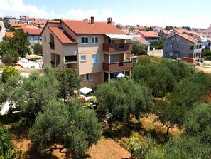 A multi-story residential building with a red-tiled roof, surrounded by dense greenery and other residential buildings in the background.