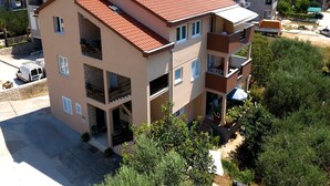 Un immeuble résidentiel à plusieurs étages, doté d’un toit recouvert de tuiles rouges, de balcons et d’un espace jardin.
