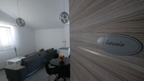 Une cuisine moderne avec un coin repas, une plaque nominative portant le nom « Antonio » et un canapé gris.
