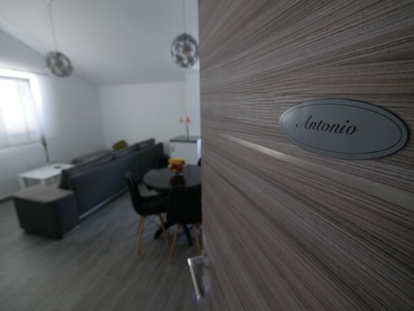 A modern kitchen with a dining area, a nameplate reading "Antonio", and a grey sofa.