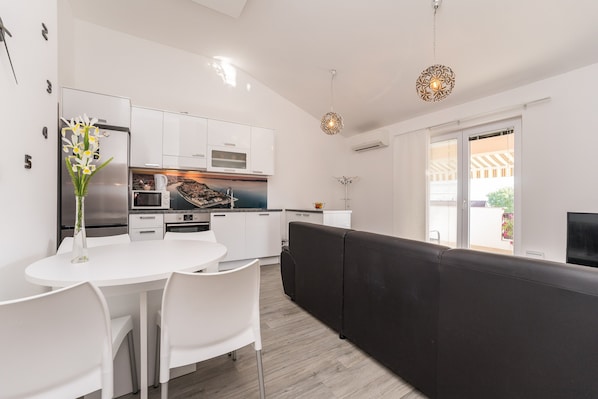 A modern kitchen with white cabinetry, a dining area with a white table and chairs, and a black sofa. - Apartments Maza - One Bedroom Apartment with Balcony (Zadar)