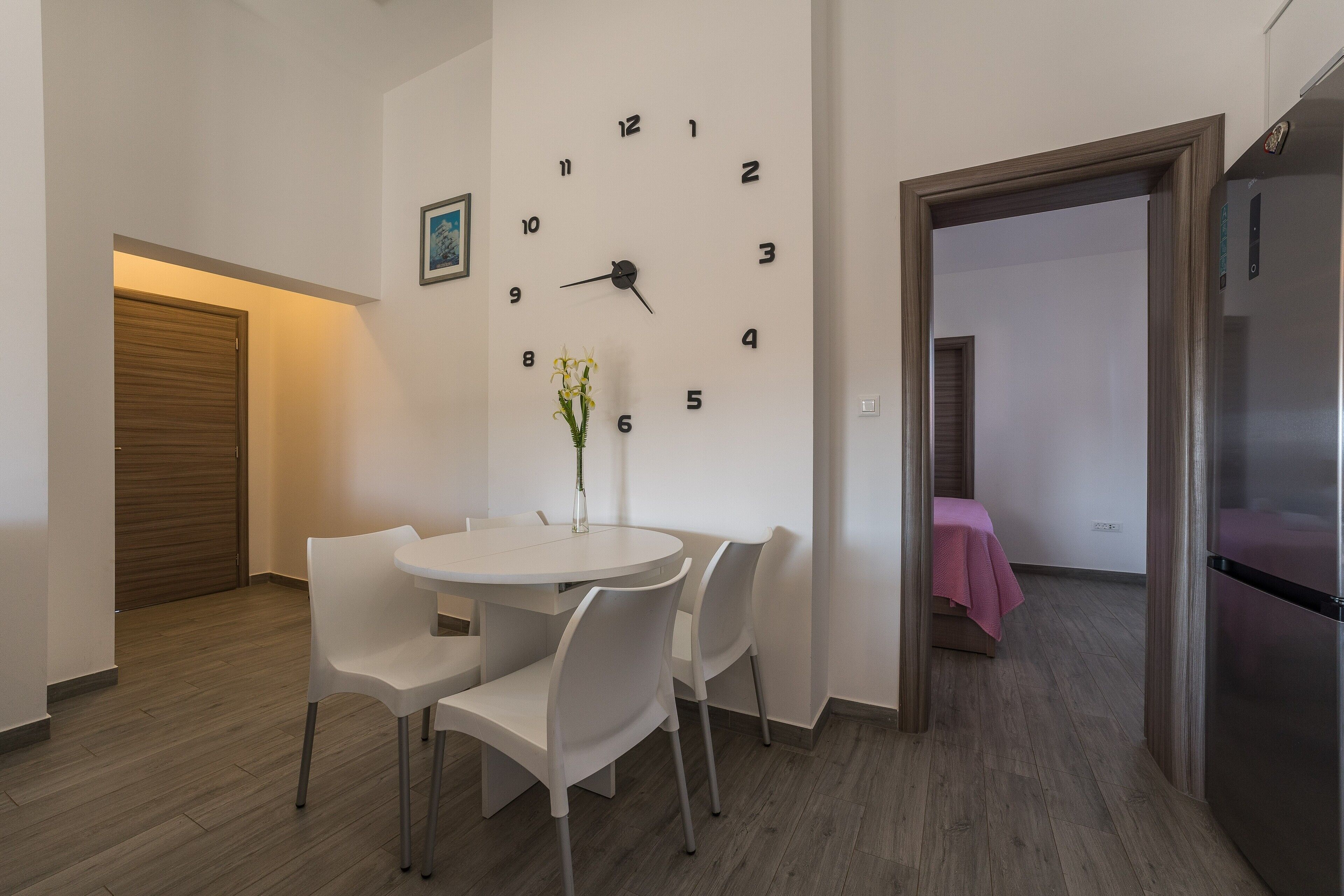 Una cucina moderna con una sveglia bianca, un tavolo da pranzo con sedie e un frigorifero.