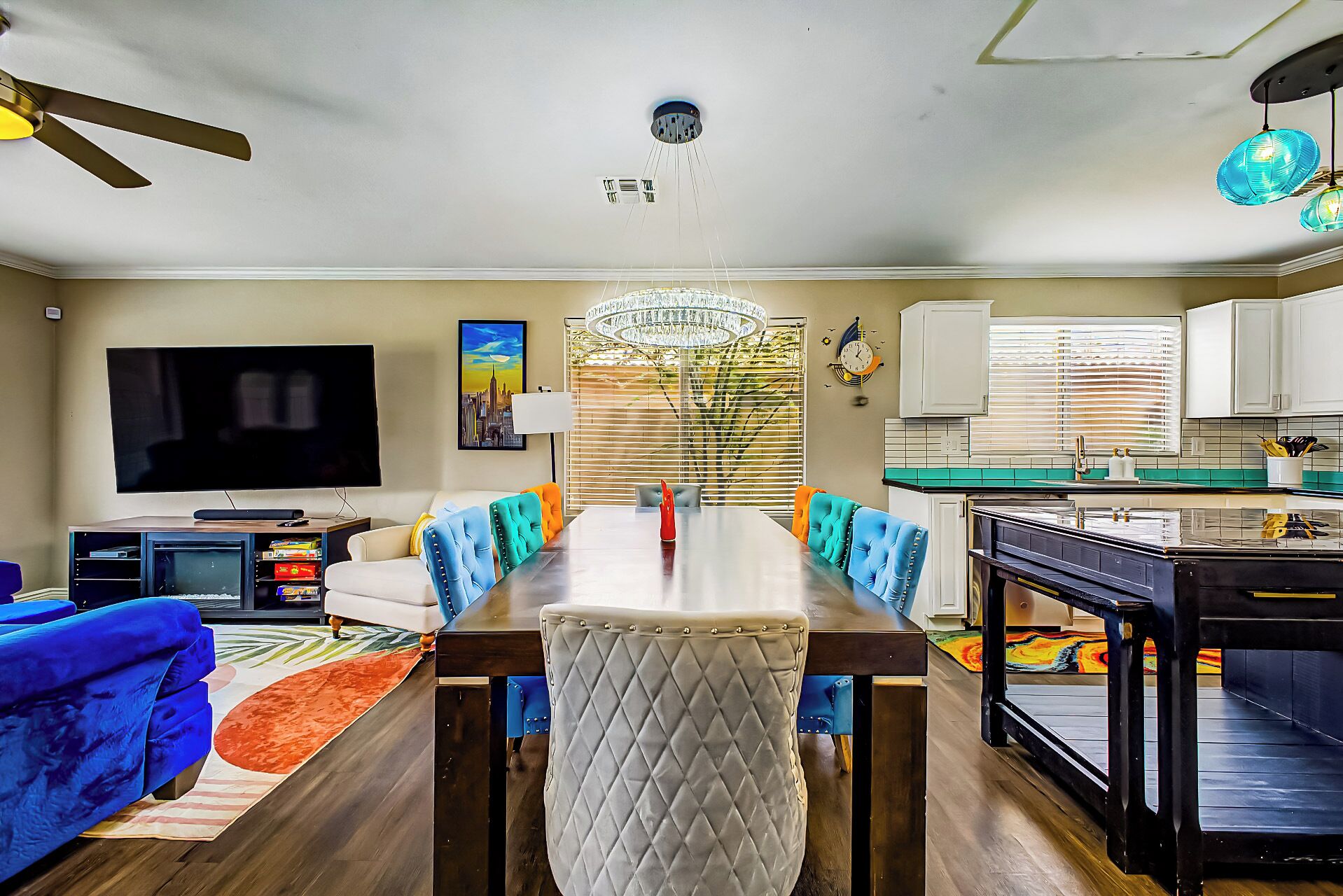 A modern living room with a dining table, sofas, a TV, and a kitchen area.