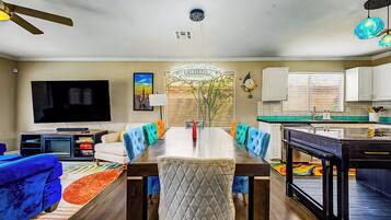 A modern living room with a dining table, sofas, a TV, and a kitchen area.