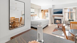 A modern hotel room with a large bed, a dining area with a table and chairs, a fireplace, and a TV mounted on the wall. - Sundial C102 | Ski-in/Ski-out | Mountain Views | Pools & Hot Tubs | Ski Valet (Park City)