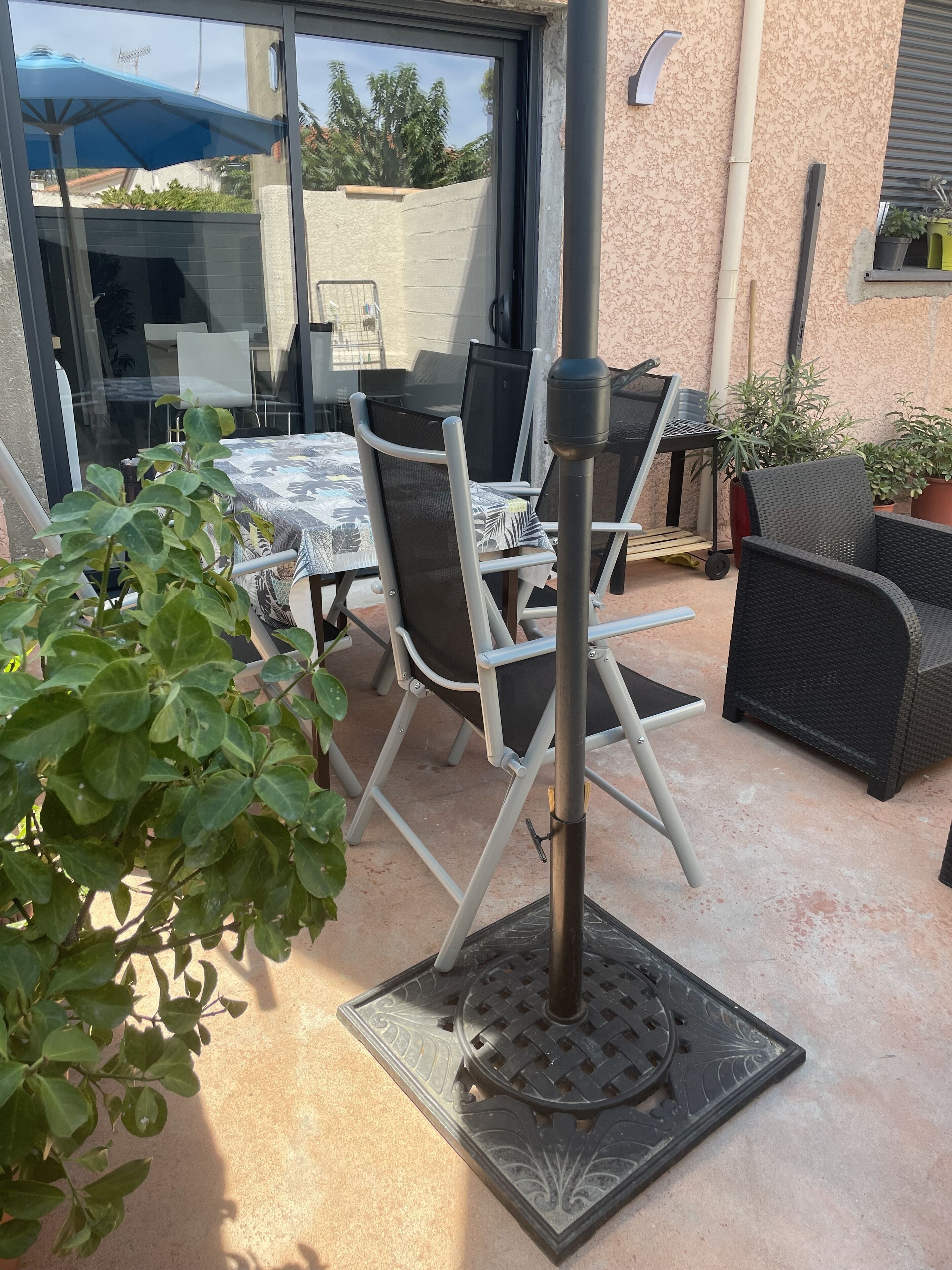An outdoor patio with a table and chairs, a metal pole, and potted plants.