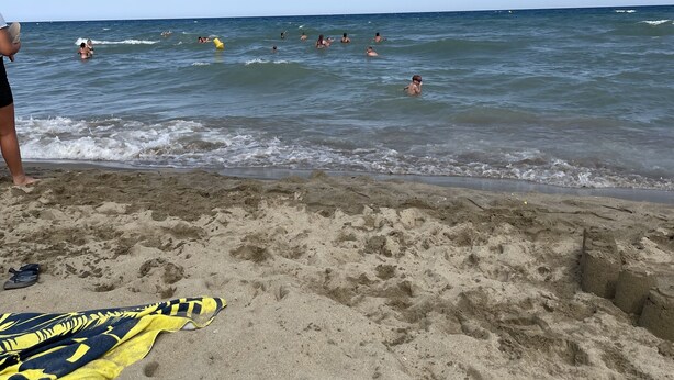 Una platja sorrenca amb empremtes i una tovallola blava i groga.