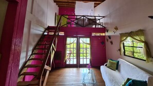 A room with a wooden staircase, a glass table with a vase, a white sofa, and a window with curtains.