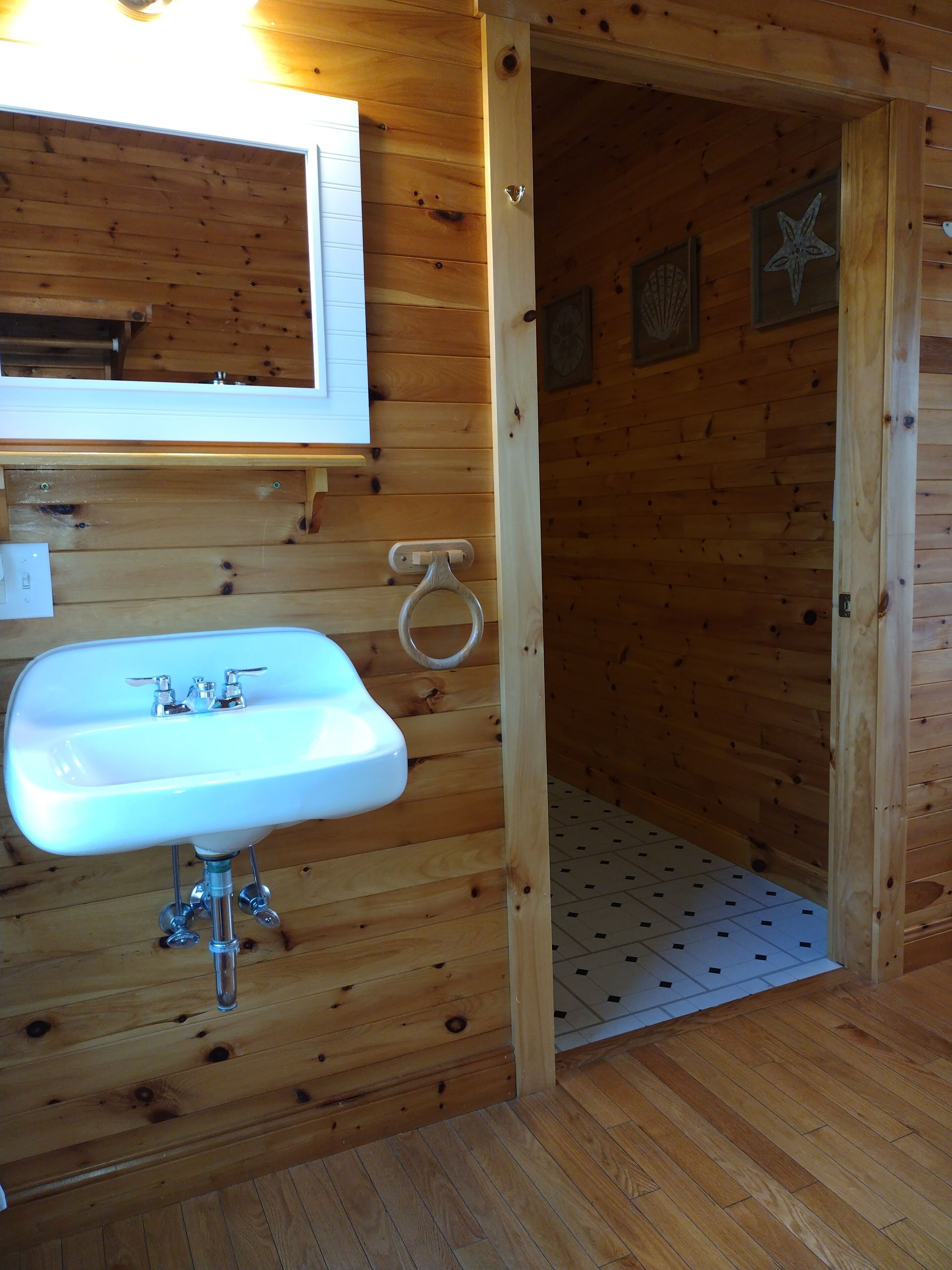 Un interno in legno con un lavandino bianco, uno specchio e una porta che dà su una zona con piastrelle.