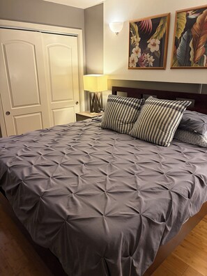 Une chambre à coucher comprenant un lit, une table de chevet, une lampe et deux tableaux accrochés au mur.