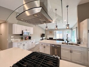 Une cuisine moderne avec des meubles blancs, des appareils en acier inoxydable et des luminaires suspendus.