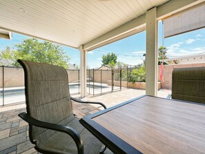 Un patio couvert avec une table et des chaises, une vue sur une piscine et un mur en briques.