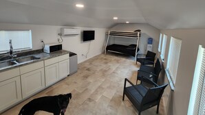 Een compacte, moderne keuken met een ingebouwde magnetron, een spoelbak en een kleine koelkast. Er staat een stapelbed met een tv erboven en er is een hond in de kamer.