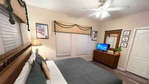 Een slaapkamer met een bed, een dressoir, een televisie en een plafondventilator.
