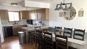 A modern kitchen with wooden cabinets, a central island, and a dining area with dark wooden chairs and a table. - Furnished Acreage by Mahoney - Sleeps 17!  Fire Pit - Shuffleboard - Clean! (Ashland)