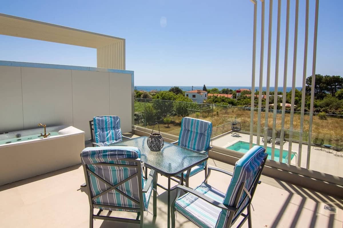 Een balkon met een glazen tafel en streepstoelen, met uitzicht op een zwembad en een schilderachtig panorama.