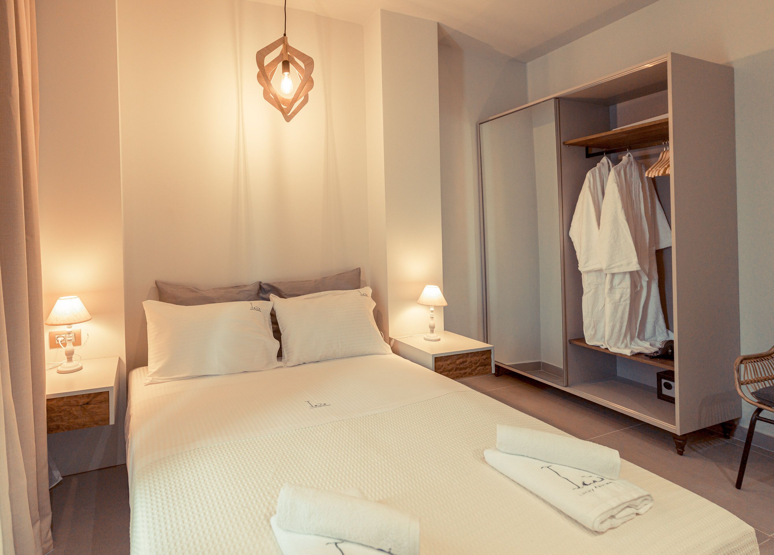 Una habitación de hotel con una cama grande, dos lámparas de noche, un armario y una silla.