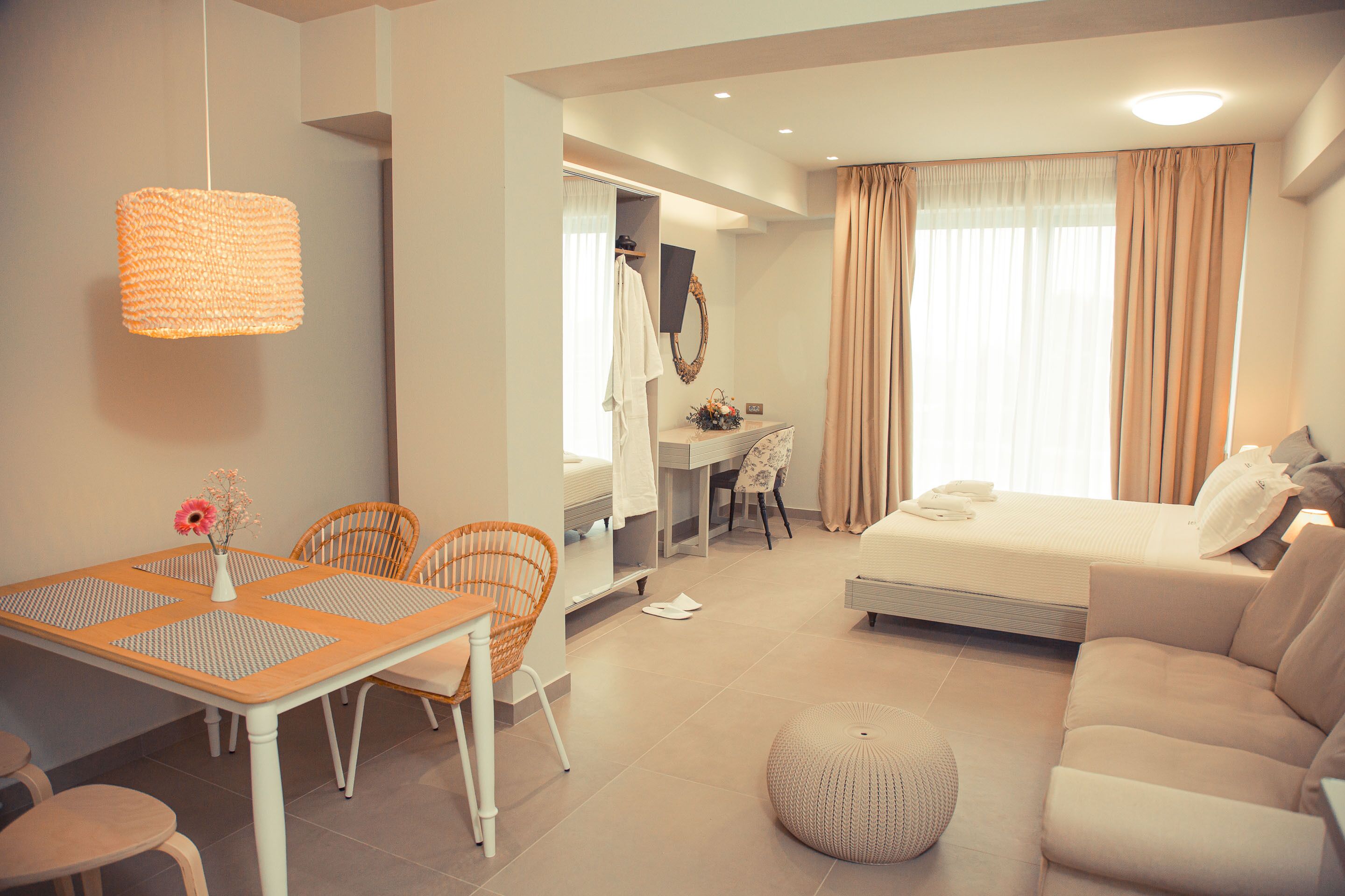 Une chambre d’hôtel moderne comprenant un coin repas, un canapé, un lit et une salle de bain visible à travers une porte ouverte.