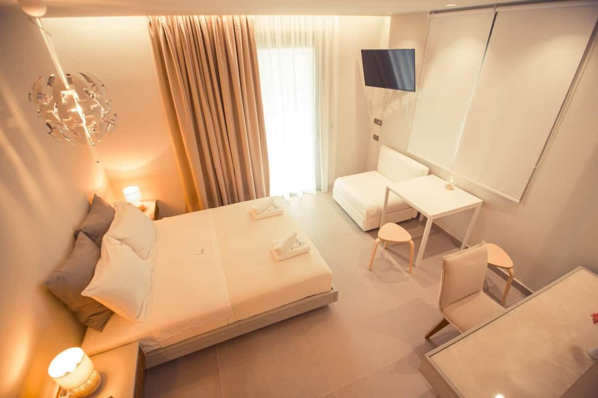 Een moderne hotelkamer met een bed, nachtkastje, bureau, stoel en een televisie aan de muur.