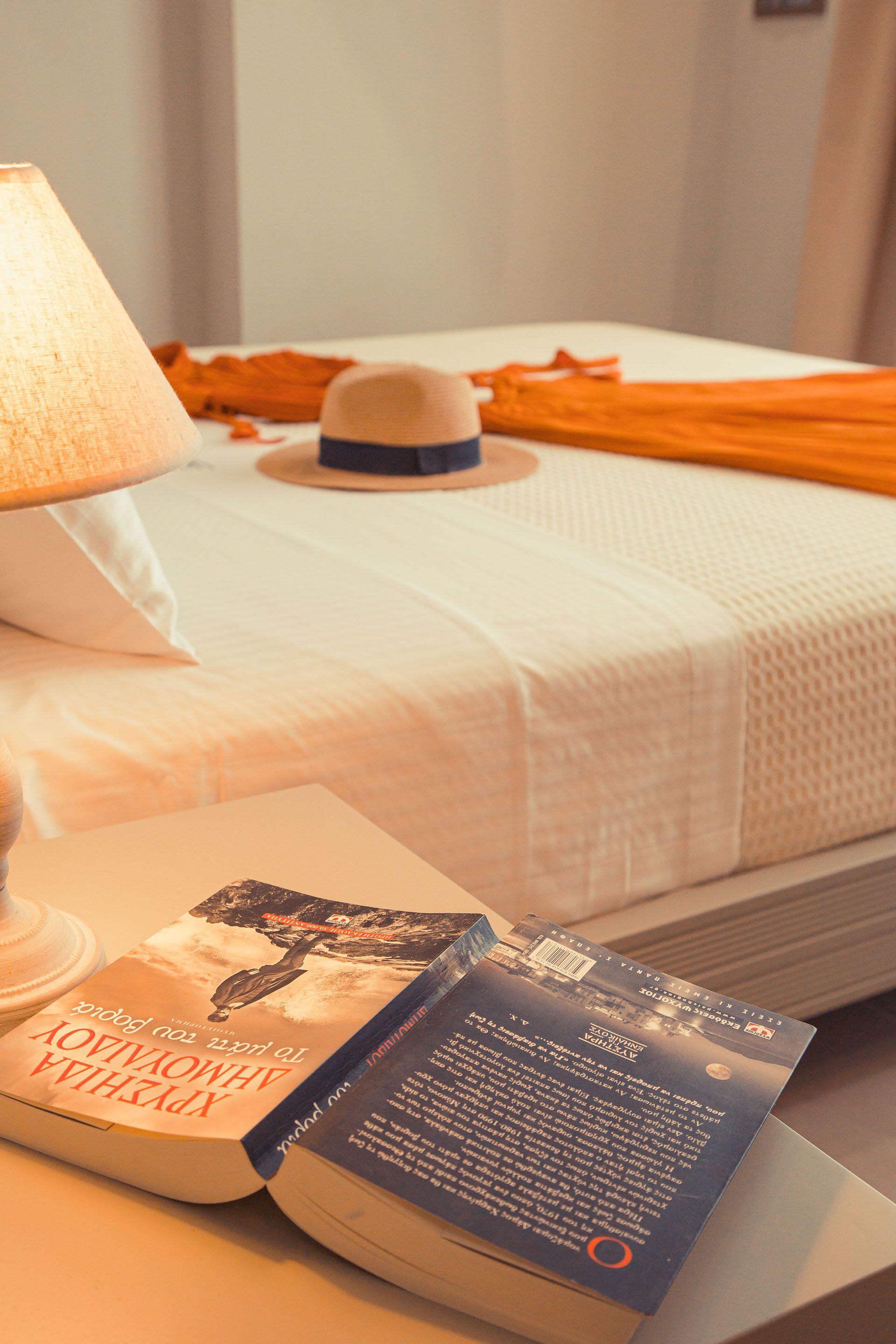 Un lit bien fait, avec une couette blanche et des rideaux orange, une lampe de chevet et un livre intitulé « Le Livre de Kells » posé sur une table de chevet.