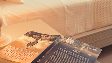 Un lit bien fait, avec une couette blanche et des rideaux orange, une lampe de chevet et un livre intitulé « Le Livre de Kells » posé sur une table de chevet.