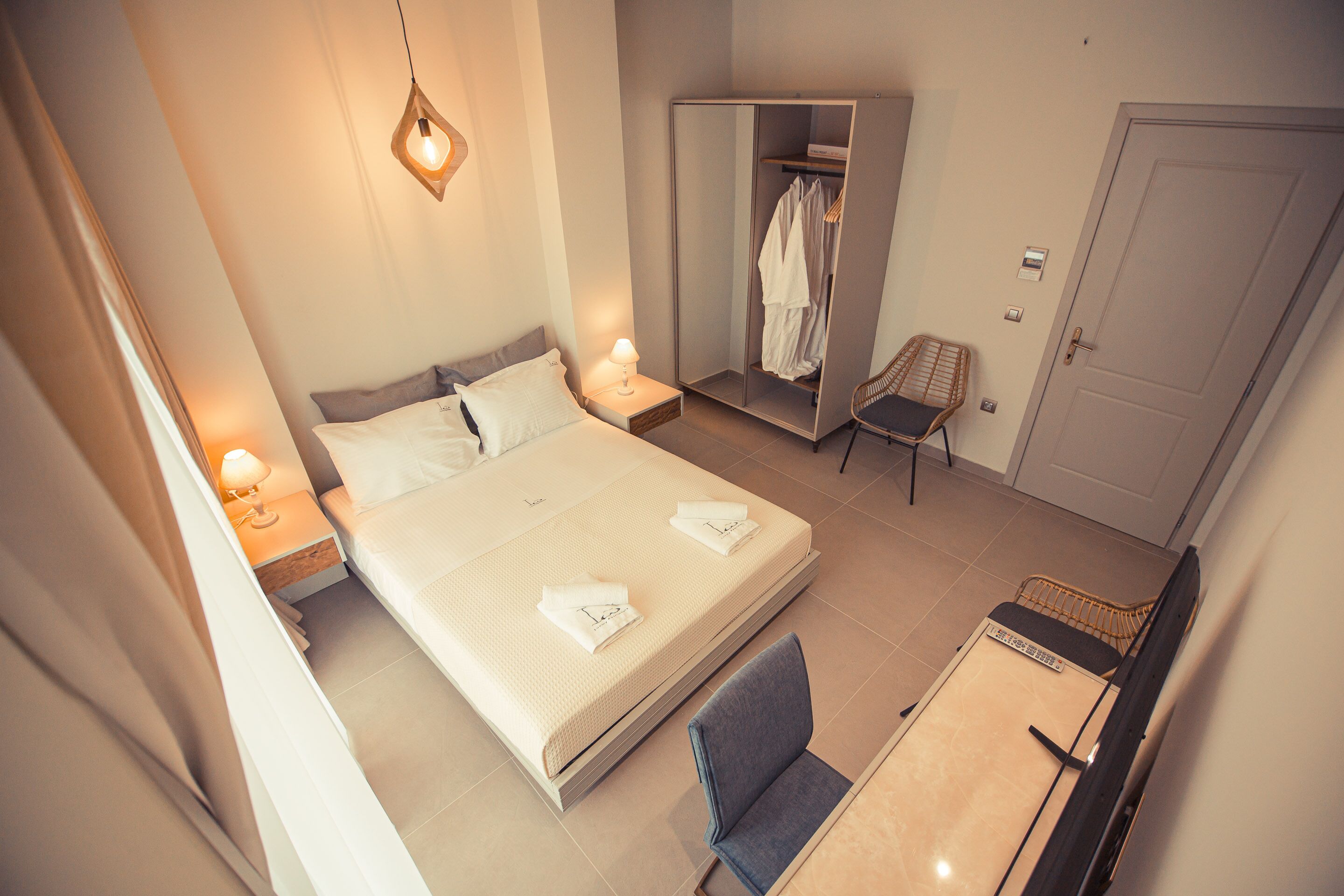 Un dormitorio ordenado con cama, mesitas de noche, una silla, un armario y una puerta.