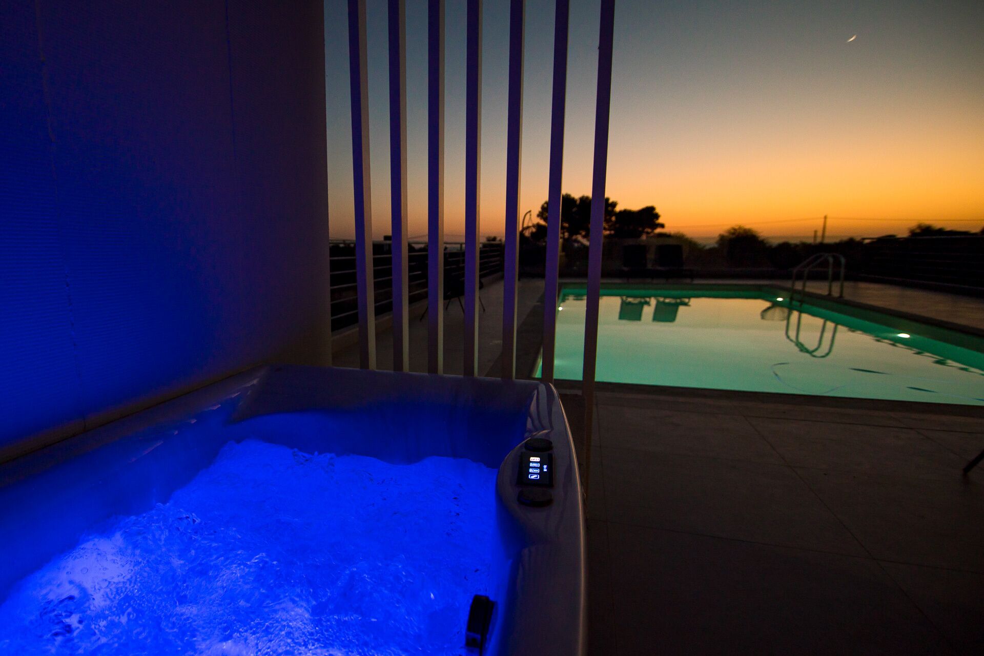 A hot tub with a control panel, a pool, and a view of the sunset.